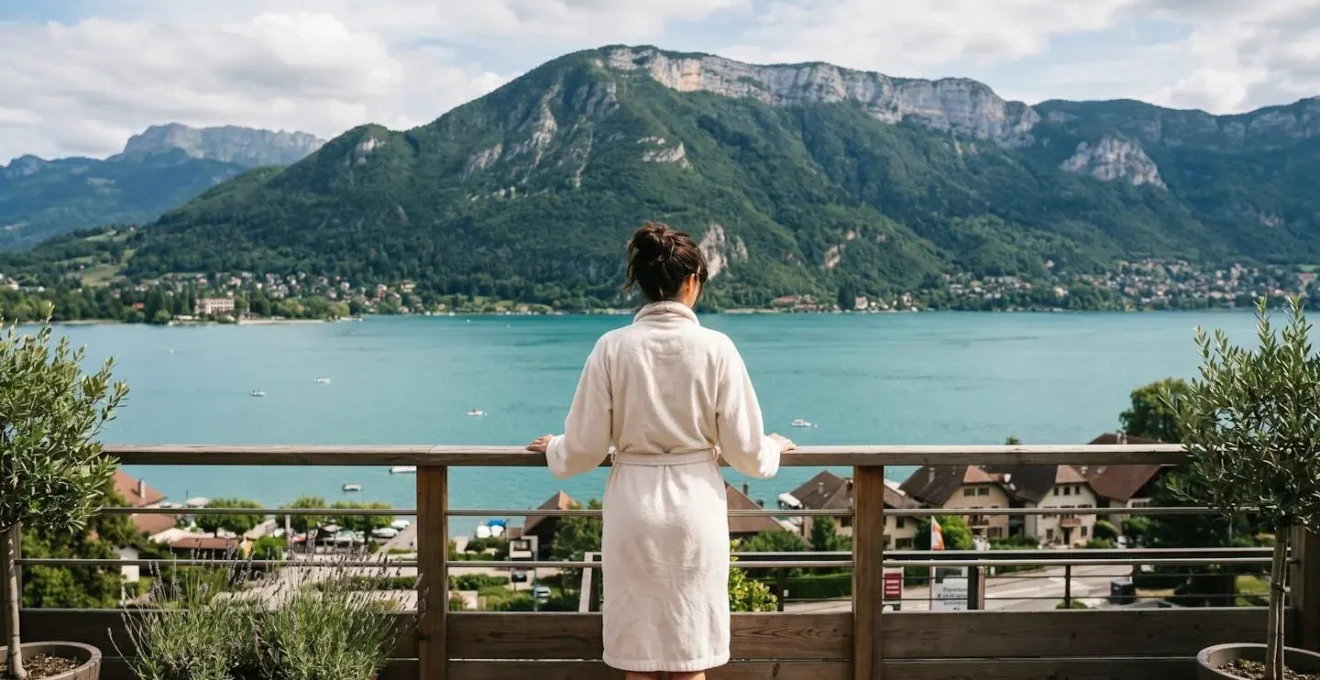 Femme en peignoir spa vue de dos regardant le panorama du lac d'Annecy depuis une terrasse bien-être, posture relaxée, montagnes en arrière-plan