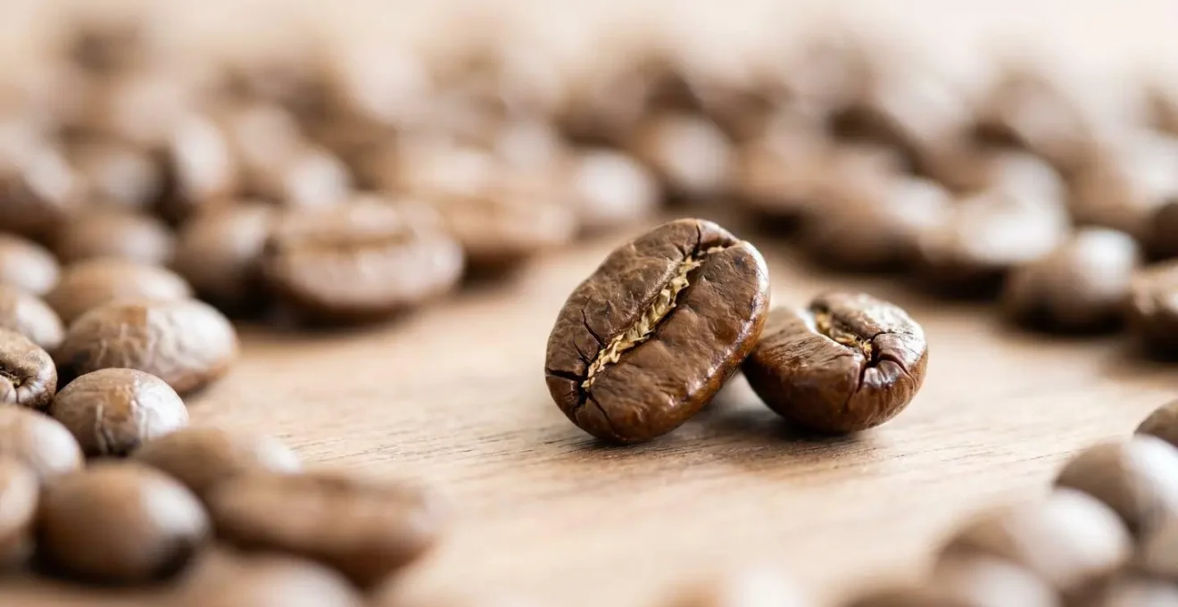 Gros plan macro sur des grains de café torréfiés dispersés sur une surface en bois clair avec détails de texture